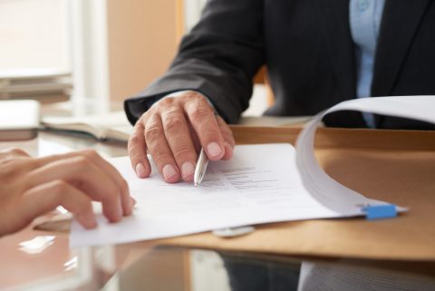 Close-up of businessman examining business contract and signing it at the office desk